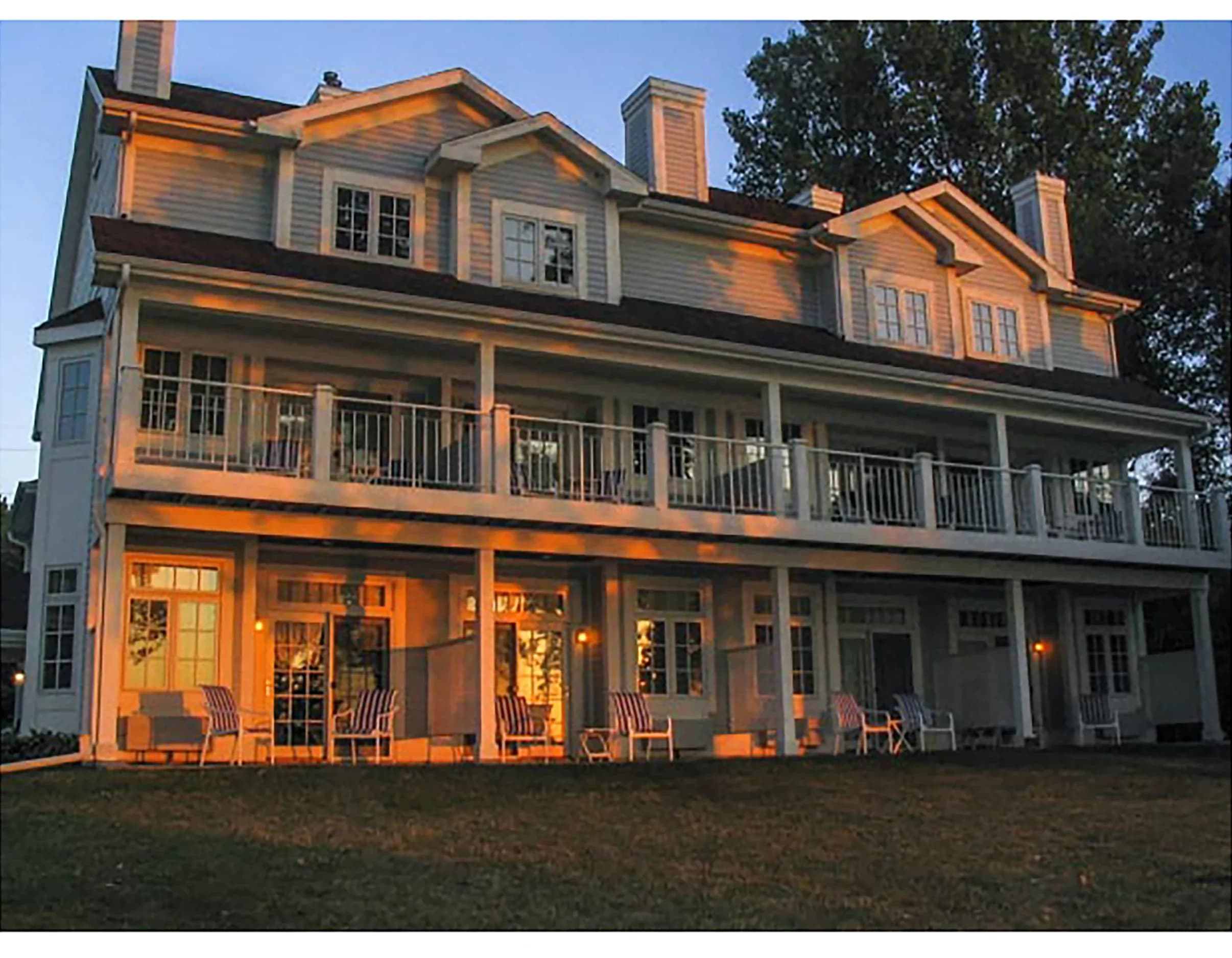 The Inn at golden hour, both porch levels lit, seen from the lawn