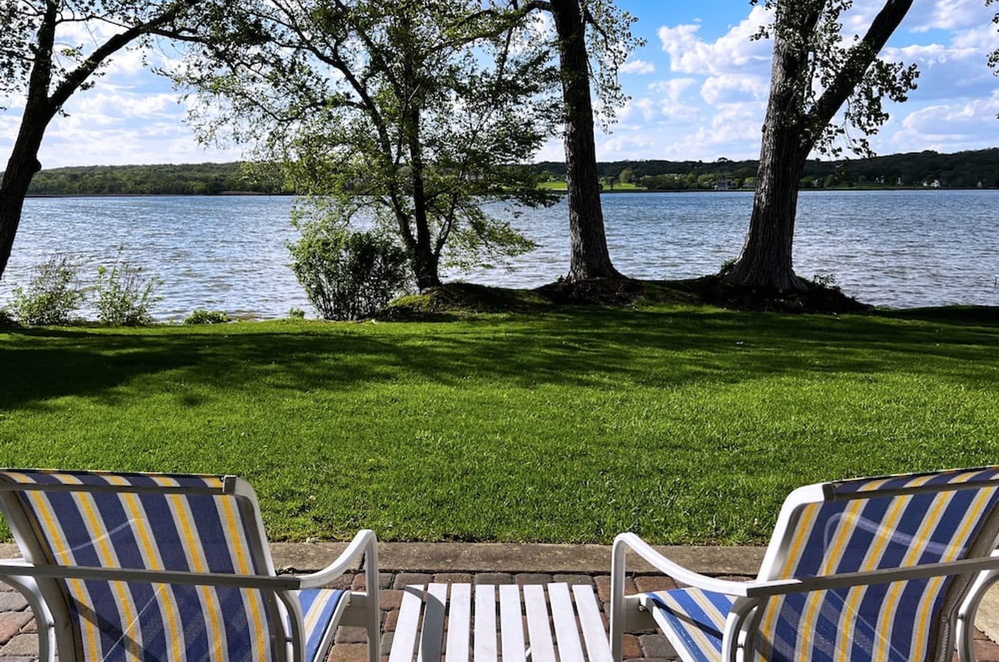 Two striped chairs on the patio, looking across the lawn to the lake