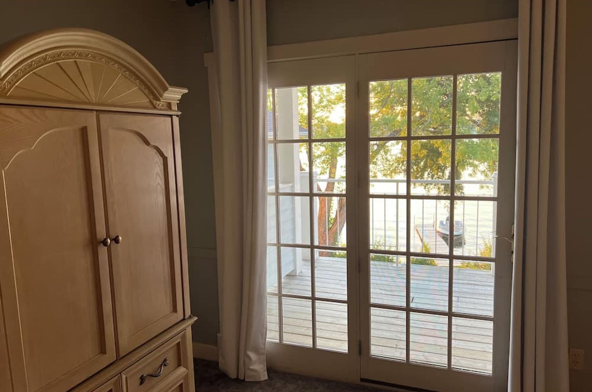 French doors open to a deck, beside a tall wooden armoire