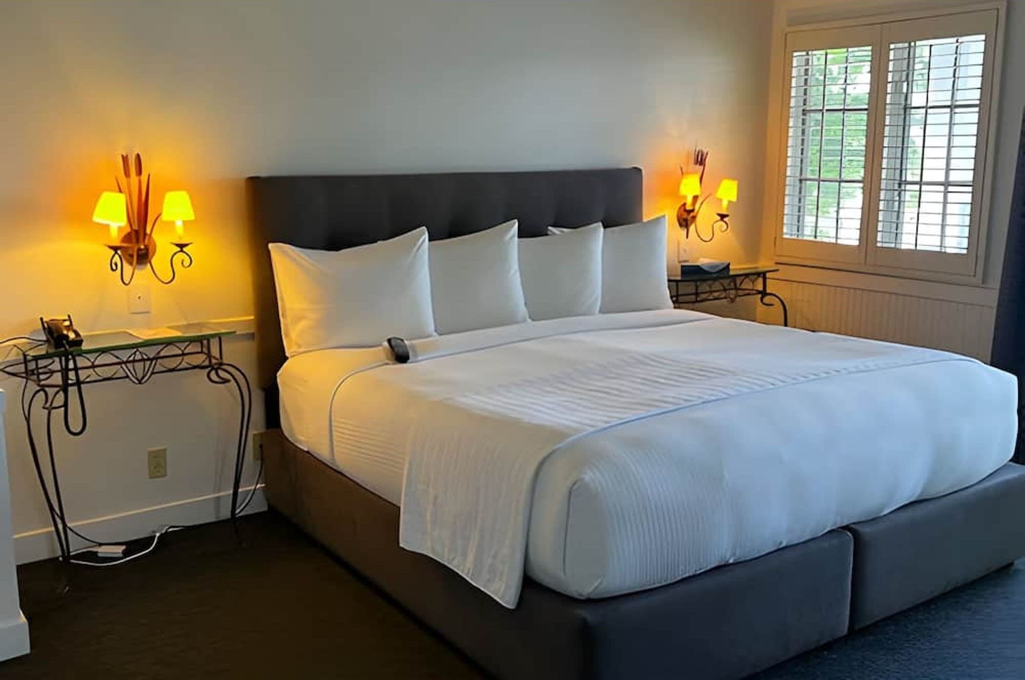 A king bed with white linens between two lit wall sconces