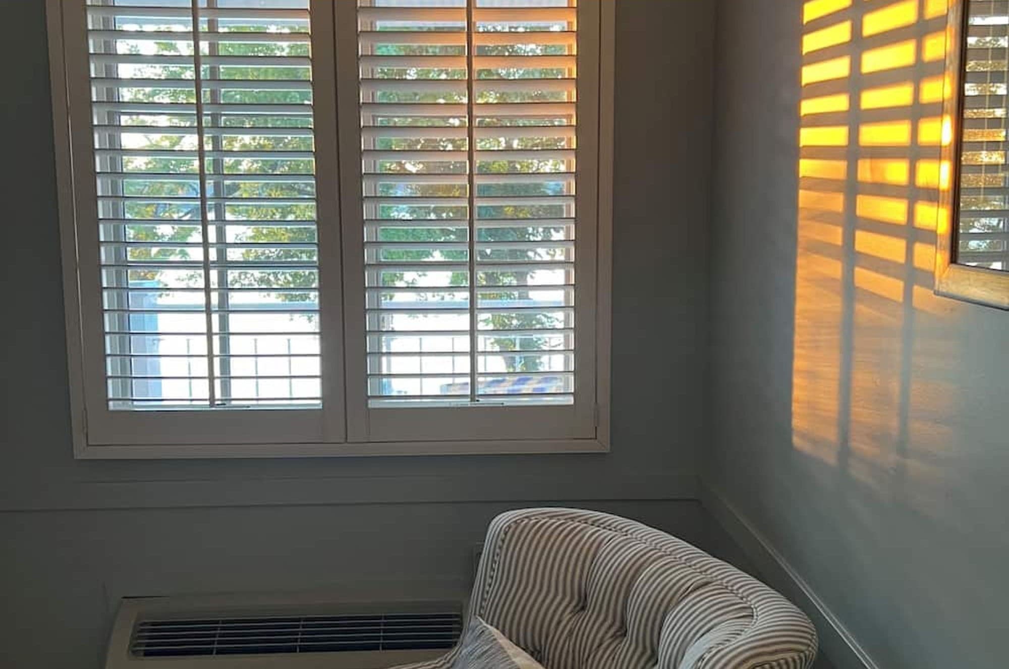 Late sun through white plantation shutters onto a striped armchair