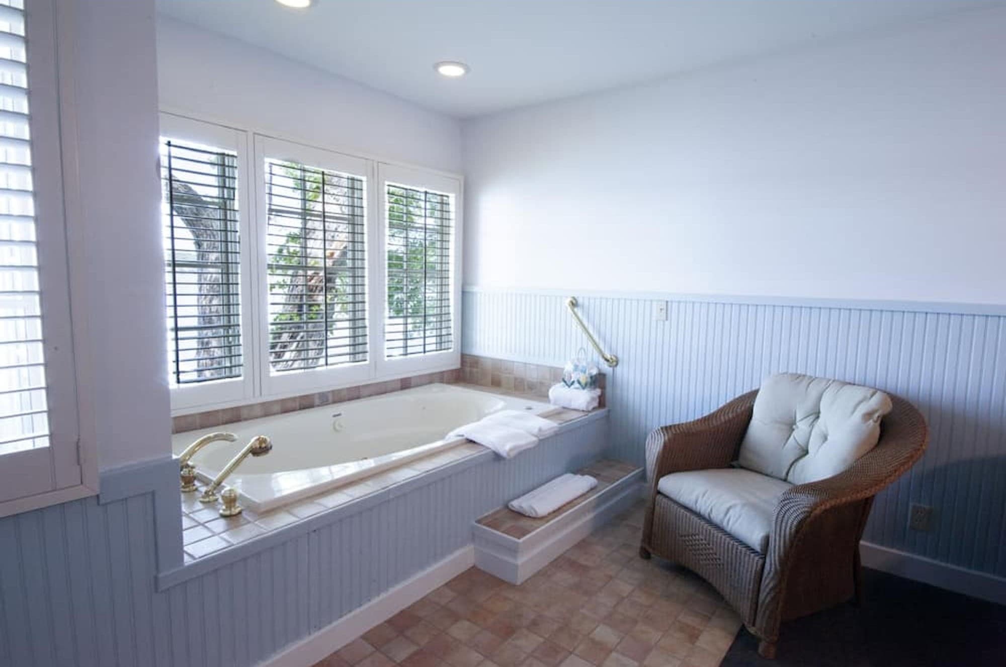 A two-person whirlpool under shuttered windows, with a wicker chair beside it